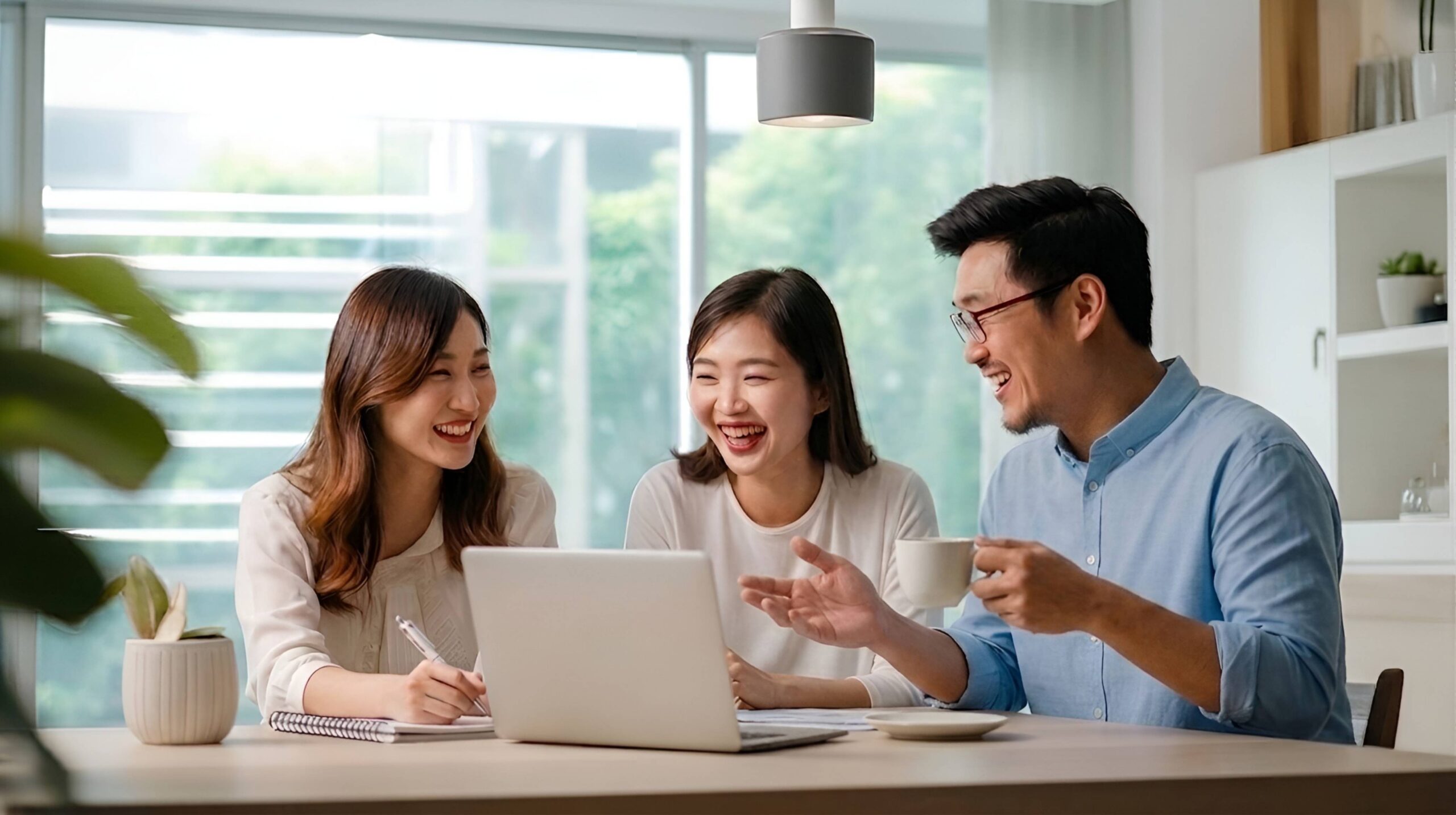 A young Singaporean couple laughing with a Havend insurance specialist during a financial planning session at a bright dining table, representing clear and independent insurance advice in Singapore.