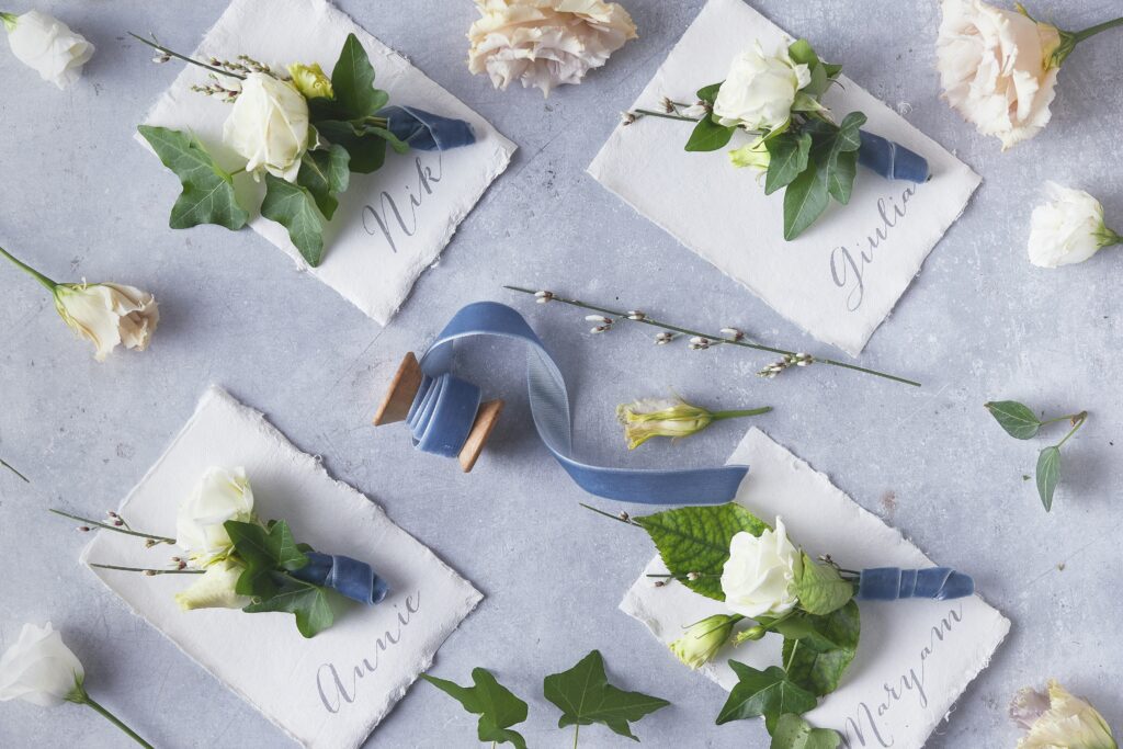 Handwritten wedding place cards with white flowers and blue ribbon — insurance planning for newlyweds in Singapore