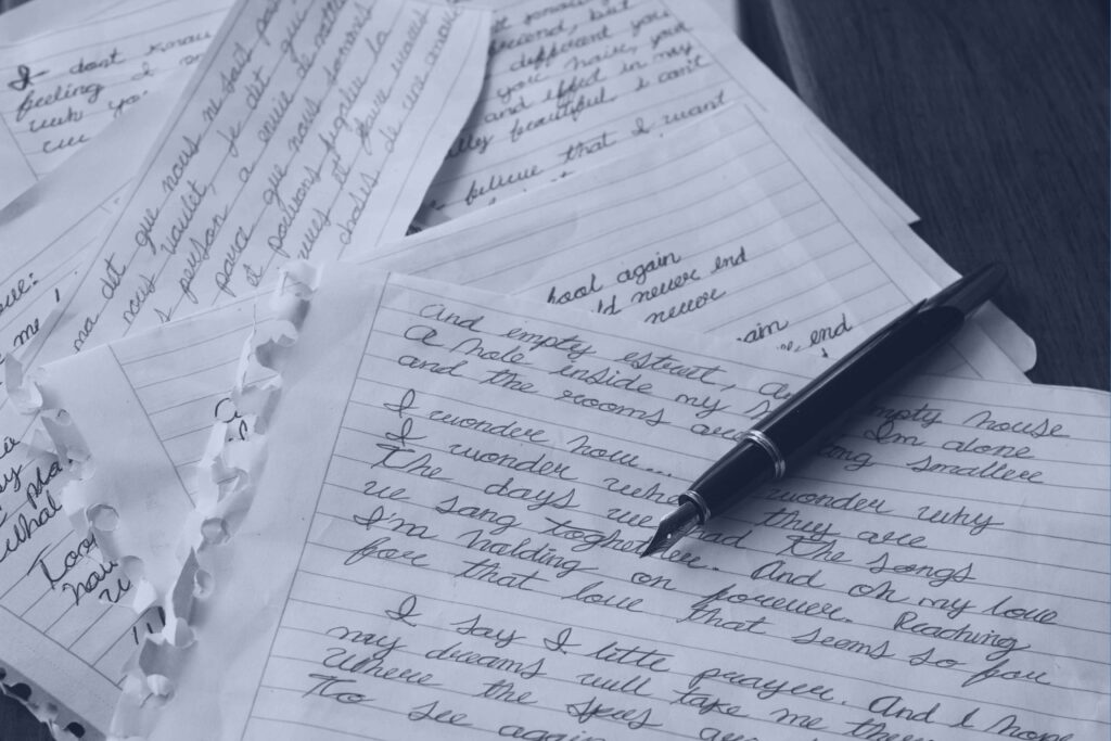 Handwritten letters spread across a desk with a black fountain pen resting on top, in a navy-toned photograph.
